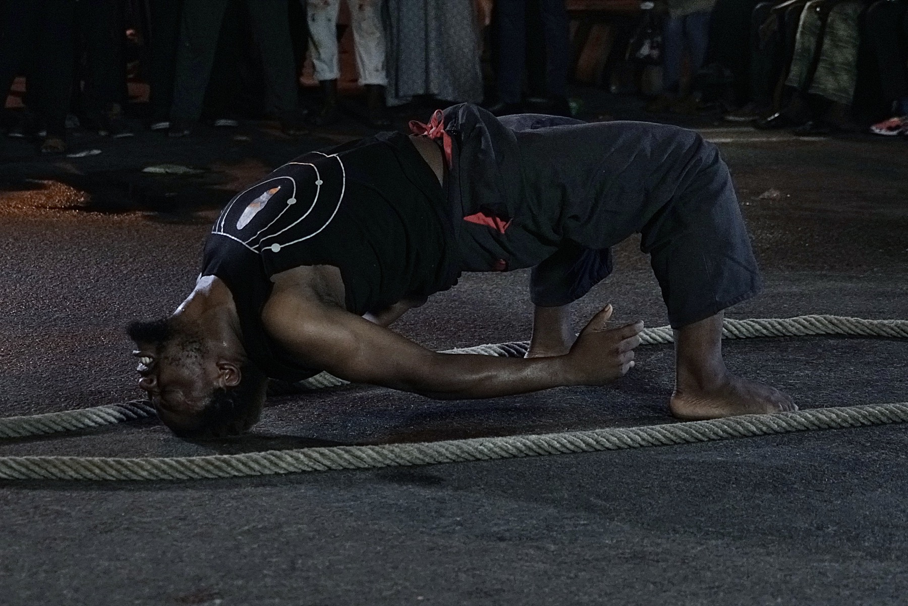 Man balancing on his head and feet on the ground between ropes