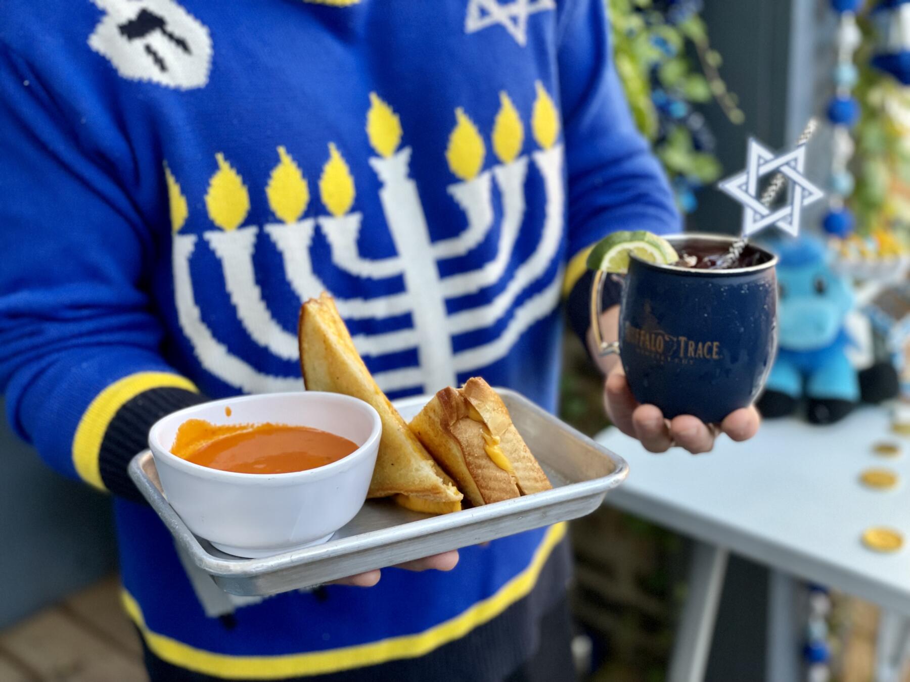 Customer in Menorah Christmas sweater holding a drink and grilled cheese with tomato soup