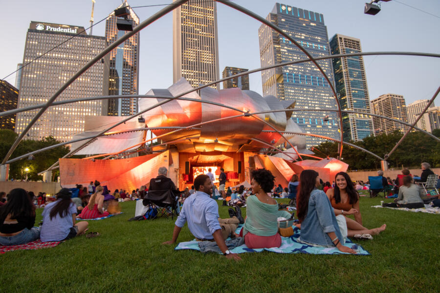 Friends watch a show in the grass at Pritzker Pavilion in Millennium Park at sunset