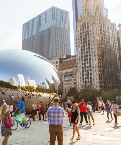 Visitors at Cloud Gate in Millennium Park with Chicago’s skyline behind. A vibrant downtown hub surrounded by hotels, art, and culture.