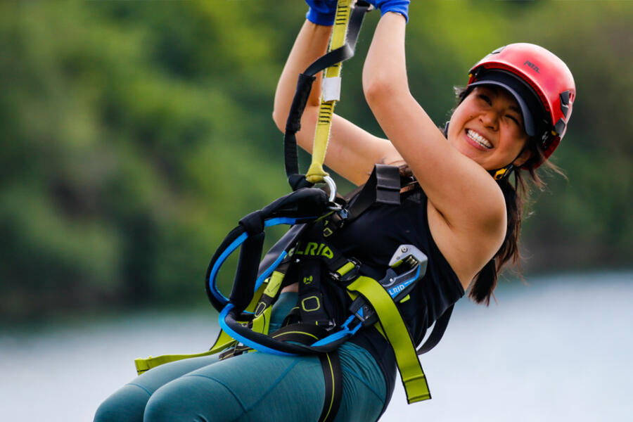 A young woman smiling while enjoying the zipline from one of the tallest ropes course towers in the world at The Forge: Lemont Quarries.