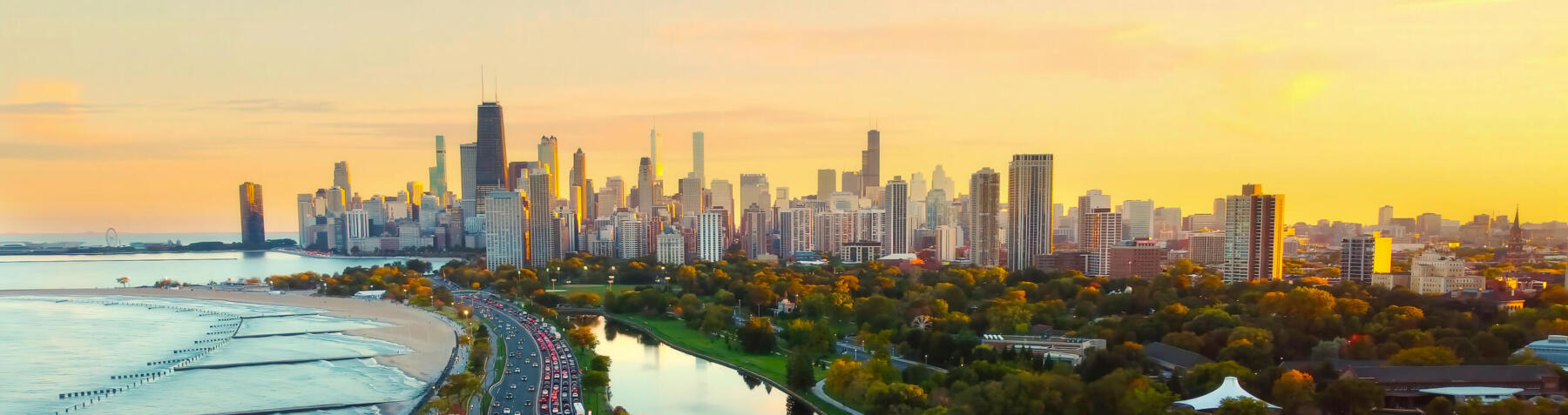 Chicago Cityscape at Sunset with Lakefront View. Aerial view of Chicago skyline at sunset, showing Lake Michigan shoreline, tree-lined parks, and a busy roadway along the waterfront.