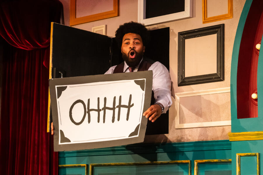 An actor on stage during The Second City sketch show, holding a sign that says OHHH