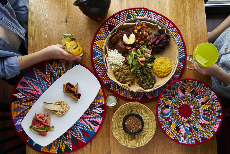 Two diners, two drinks and colorful platters holding food on a table inside Demera Ethiopian Restaurant in the Uptown neighborhood of Chicago