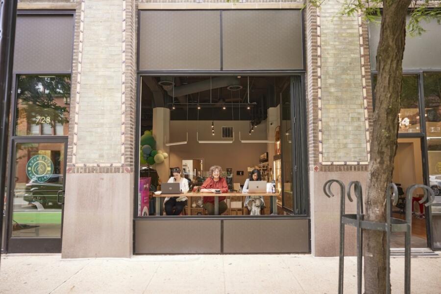 View from the sidewalk of three people sitting inside working on laptops looking out a window of , necessary & sufficient coffee®