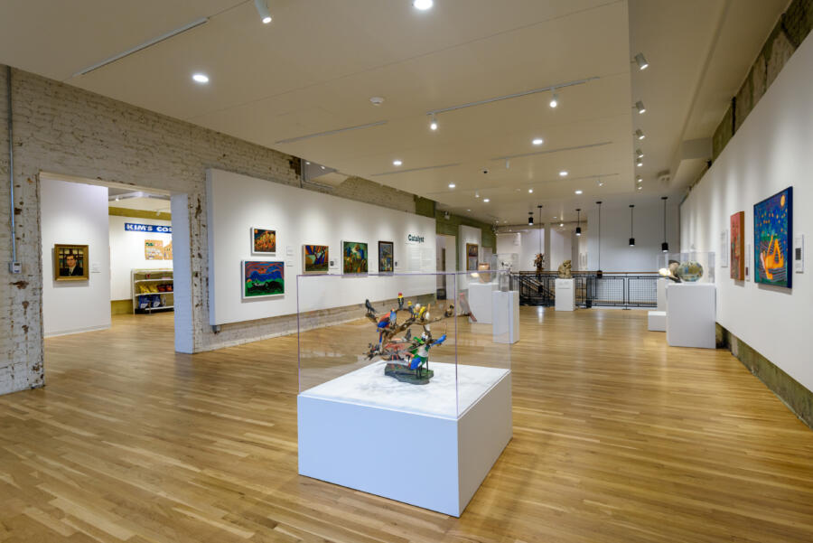 A view of colorful paintings hanging on walls and artwork enclosed in inside glass boxes inside the Intuit Art Museum in Chicago