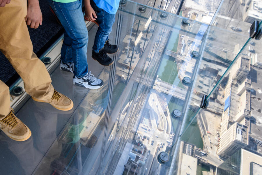 A group of tourists stand on The Ledge at Skydeck Chicago and look down at the city.