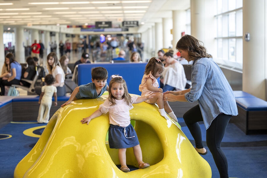 Adults supervise children playing on colorful equipment in the Kids Play Area at Chicago Midway International Airport