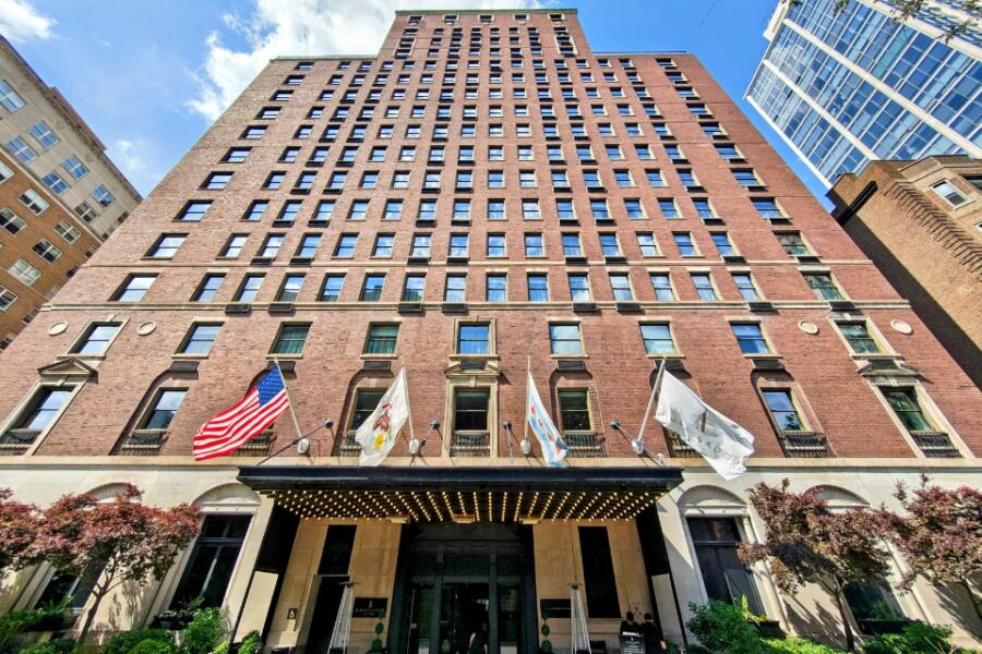 Low-angle exterior of the Ambassador Chicago hotel, a tall brick building with an awning entrance and flags out front.