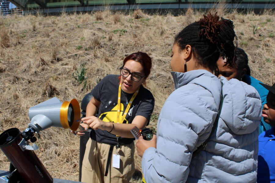 Adler Planetarium staff member pointing to a solar telescope with visitors watching outdoors.