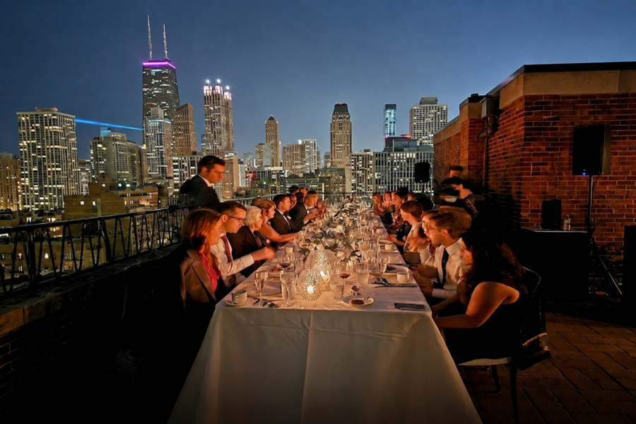 Rooftop dinner party at night with the Chicago skyline lit up behind the guests.