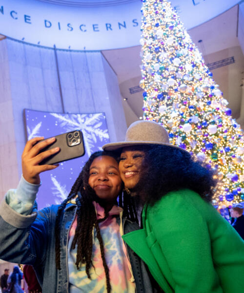 Two friends take a selfie in front of a Christmas tree at the Christmas Around the World at Museum of Science and Industry.