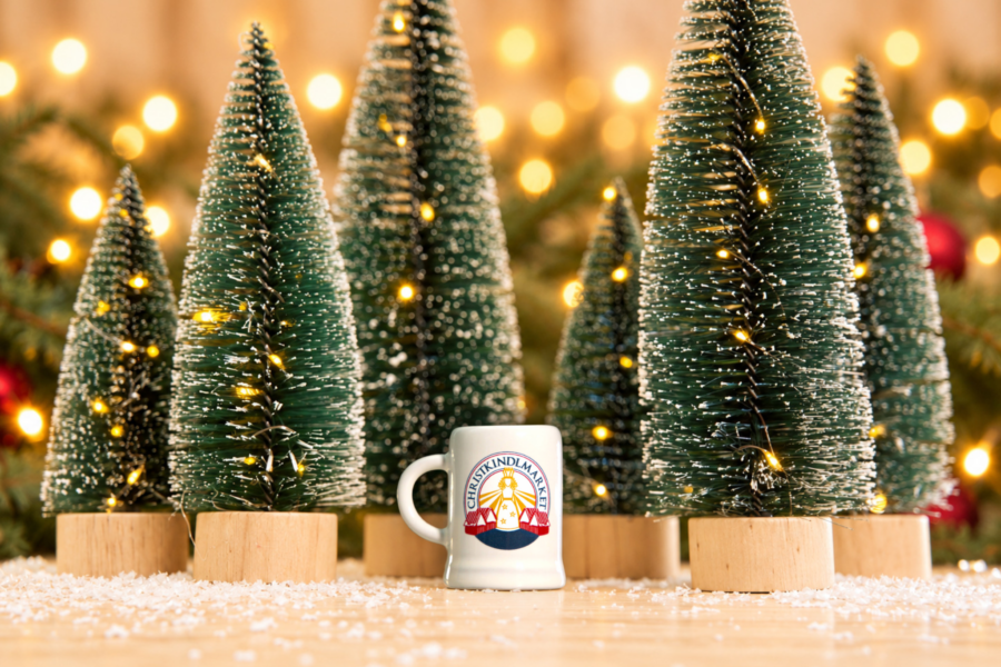Small white Christkindlmarket Mini Stein Shot Cup 2026 placed next to mini Christmas trees.